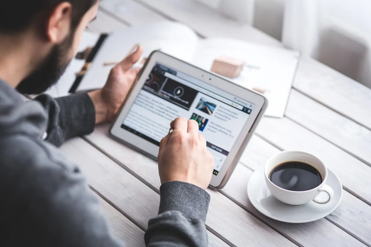 Internaute consultant un site internet et un article de blog sur une tablette avec un café
